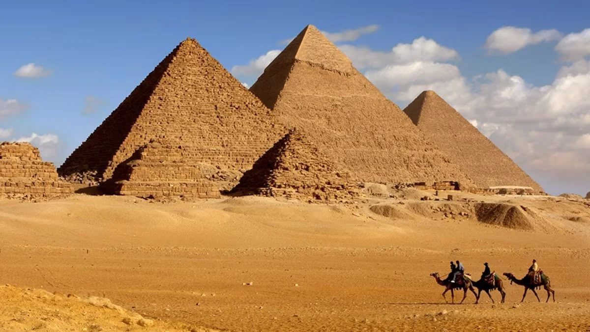A camel caravan crossing the desert below the pyramids of Giza