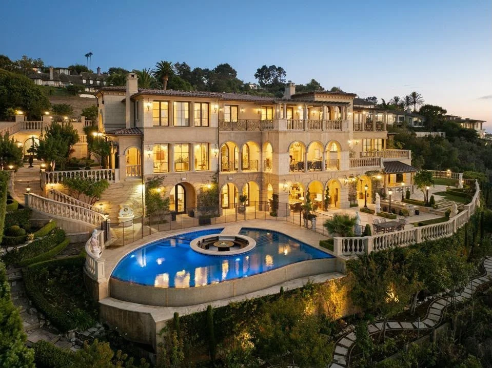 A hillside villa with a lit pool at dusk