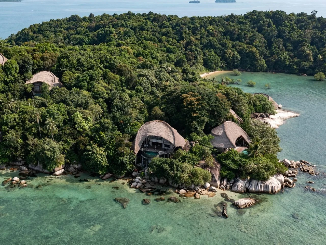 A wooded island with private villas above clear turquoise water